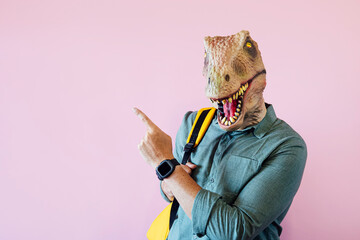 Man with lizard mask on pink background pointing to the side.