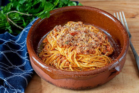 A terracotta bowl with spaghetti "alla chitarra" with tomatoes sauce and parmesan cheese.