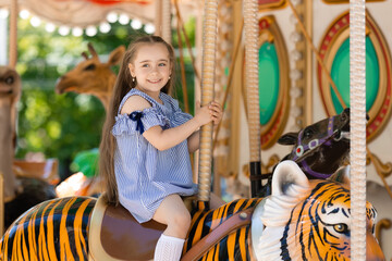 Fototapeta na wymiar Adorable little girl in blue dress at amusement park having a ride on the merry-go-round