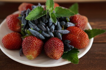 berries of red fresh strawberries and blue honeysuckle with green mint leaves in a white plate on a...
