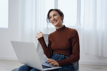 Excited cheerful happy enthusiastic shocked curly awesome young woman talks with friend in video conference call tells about latest cool news holds laptop raise hand active gesturing in chair at home