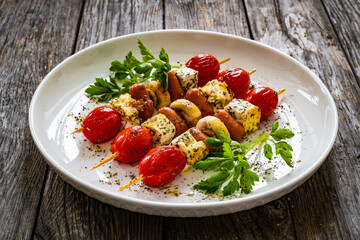 Sausage skewers - fried sausages with feta cheese, mushrooms and cherry tomatoes on wooden table
