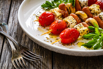 Sausage skewers - fried sausages with feta cheese, mushrooms and cherry tomatoes on wooden table
