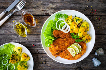 Breaded fried pork chop with fried potatoes and greens on wooden table

