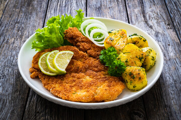 Breaded fried pork chop with fried potatoes and greens on wooden table

