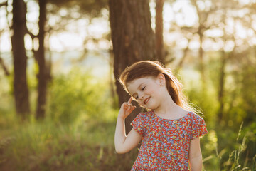 Fototapeta premium A little girl in a white dress and sandals runs along a country road. She holds a toy in her hands. Happy childhood. Summer vacation