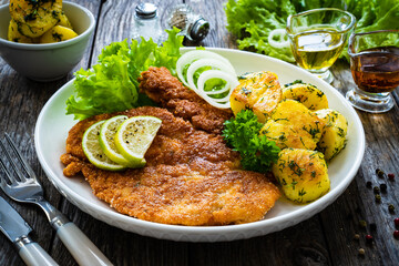 Breaded fried pork chop with fried potatoes and greens on wooden table

