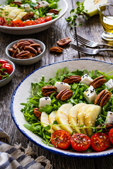 Fresh salad - goat cheese, pear and vegetables on wooden table
