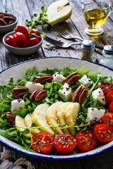 Fresh salad - goat cheese, pear and vegetables on wooden table
