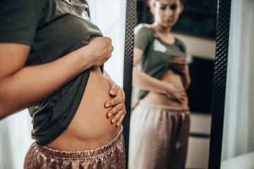 Woman Touching Her Belly While Standing Near Mirror