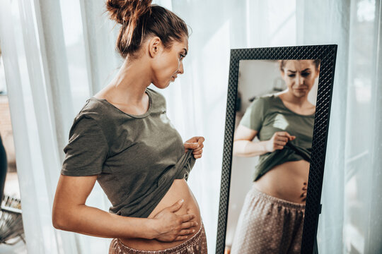 Woman Touching Fat Belly While Standing Near Mirror