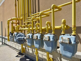 Nature gas cubic meters in a row with yellow gas supply pipes on exterior wall of building. Energy...
