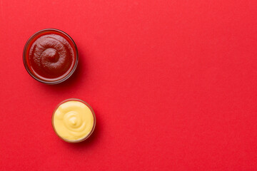 Bowl of ketchup and cheese sauce on colored background, top view with copy space