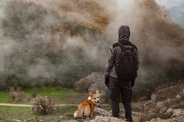 A man and a Pembroke Welsh Corgi climb above the clouds high in the mountains.