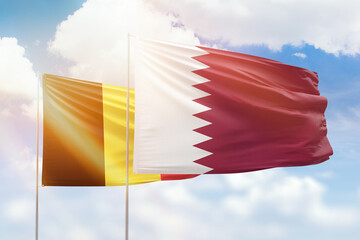 Sunny blue sky and flags of qatar and belgium