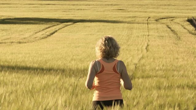 Slow motion of a young caucasian mature woman running inside a barley field in spring seen from behind.  4K. Ayegui, Navarre, Spain, Europe.
