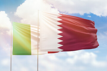 Sunny blue sky and flags of qatar and italy