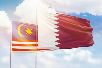 Sunny blue sky and flags of qatar and malaysia