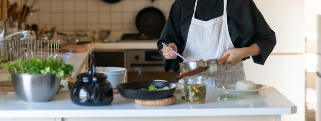 キッチンで料理をするエプロン姿の女性　皿に料理を盛り付ける	