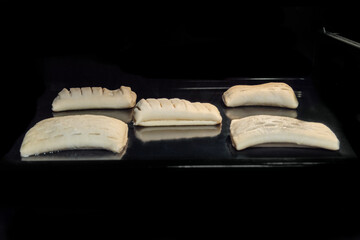 Five uncooked puff pastry buns with fruit jam on tray in electric oven, black background. Homemade bakery, food, cooking, pastry, semi-finished products and raw concept