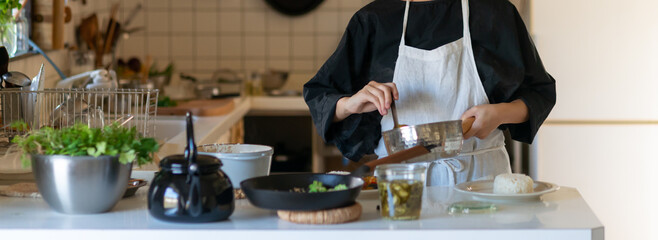 キッチンで料理をするエプロン姿の女性　皿に料理を盛り付ける - obrazy, fototapety, plakaty