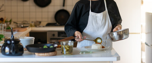 キッチンで料理をするエプロン姿の女性　皿に料理を盛り付ける