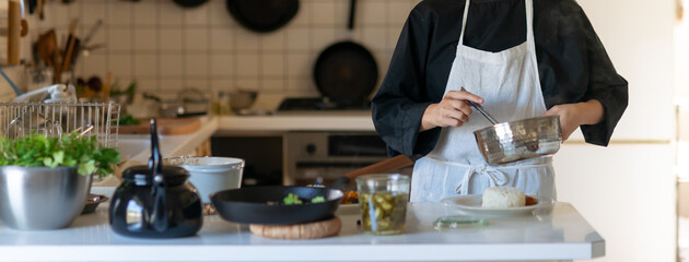 キッチンで料理をするエプロン姿の女性　皿に料理を盛り付ける
