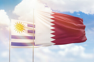 Sunny blue sky and flags of qatar and uruguay