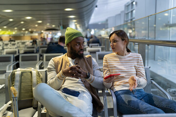 Interracial friends waiting for flight at airport lounge, talking and discussing travel plan. Young...