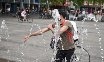 a bike courier with a bike refreshing at a public well during the summer heat in a city, heat dome