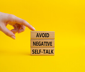 Avoid negative self-talk symbol. Concept words Avoid negative self-talk on wooden blocks. Beautiful yellow background. Bisinessman hand. Business and Avoid negative self-talk concept. Copy space.