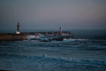 An ocean pier with a lighthouse after sunset.