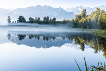 Perfect reflection in Lake Matheson surrounded by beautiful natural forest under blue sky