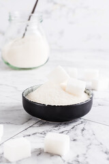 Granulated sugar and sugar cubes in a bowl and sugar in a jar on the table. Vertical view
