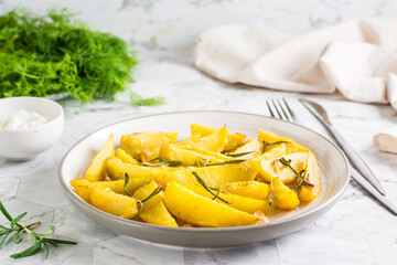 Baked potatoes with garlic and rosemary on a plate and a bowl with sauce on the table.