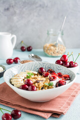 Granola with cherry, banana and flax seeds in a bowl and a jar of granola on the table. Vertical view