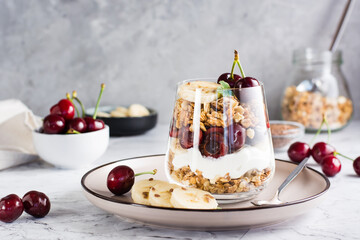 Granola with Greek yogurt, cherry and banana in a glass on the table. Homemade healthy breakfast