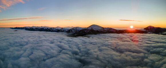 Fototapeta na wymiar Aerial view of vibrant sunrise over white dense fog with distant dark Carpathian mountains on horizon