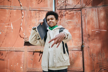 Portrait of African American skater boy holding skateboard and gesturing at camera in urban area outdoors © Seventyfour
