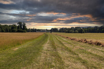 Meadow in front of Pohansko castle. Hay is being harvested in the meadow. There are dramatic clouds in the sky.