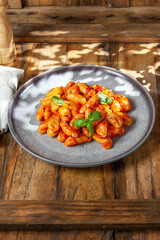 Close up of Italian potato Gnocchi with tomato sauce and fresh basil on gray plate on wooden background.