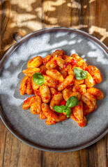 Close up of Italian potato Gnocchi with tomato sauce and fresh basil on gray plate on wooden background.