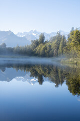 Perfect reflection in Lake Matheson surrounded by beautiful natural forest under blue sky