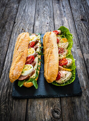 Long sandwiches with sausage, ham, chicken breast, boiled eggs, lettuce, arugula yellow cheese, tomato and dressing on wooden table
