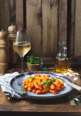 Traditional Italian potato Gnocchi with tomato sauce and fresh basil with glas of white wine. rustic background