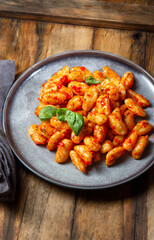 Traditional Italian potato Gnocchi with tomato sauce and fresh basil on blue plate on wooden background.