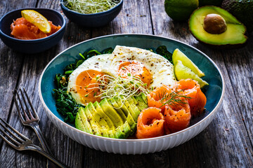 Salmon salad - smoked salmon, sunny side eggs, avocado and spinach on wooden table
