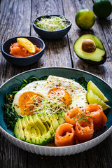 Salmon salad - smoked salmon, sunny side eggs, avocado and spinach on wooden table
