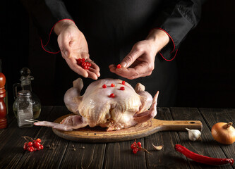 Chef prepares raw chicken in the kitchen. The cook puts the red viburnum on the chicken before baking