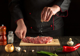 The chef or cook salting raw veal in the kitchen. Asian cuisine. Recipe idea for a hotel